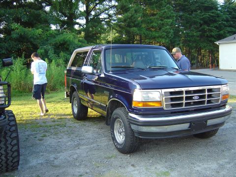 1986 Ford Bronco - Dark blue Ford Bronco parked outdoors with another vehicle partially visible on the left.