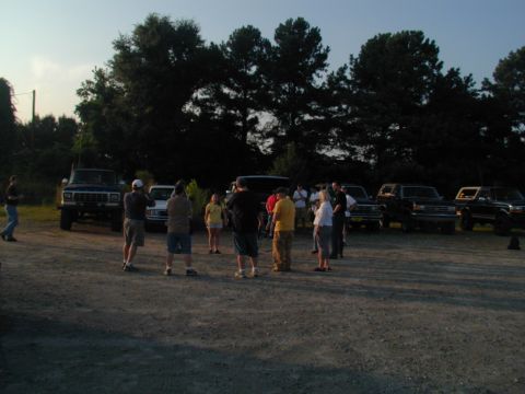 1988 Ford Bronco - Several SUVs are parked in a lot with a group of people gathered around them.
