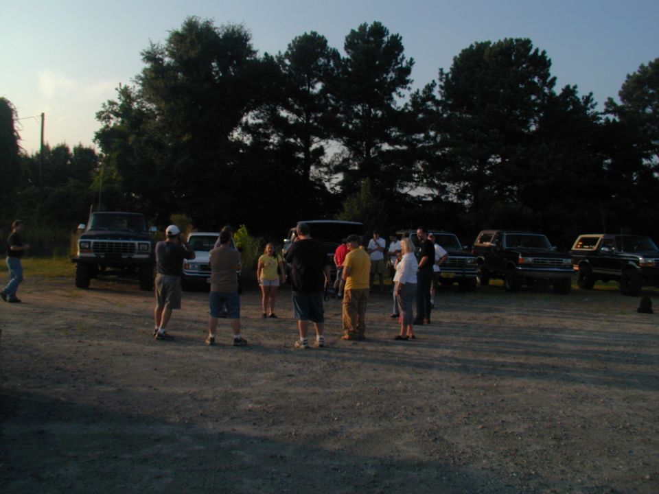 group of people standing around several SUVs in a gravel lot