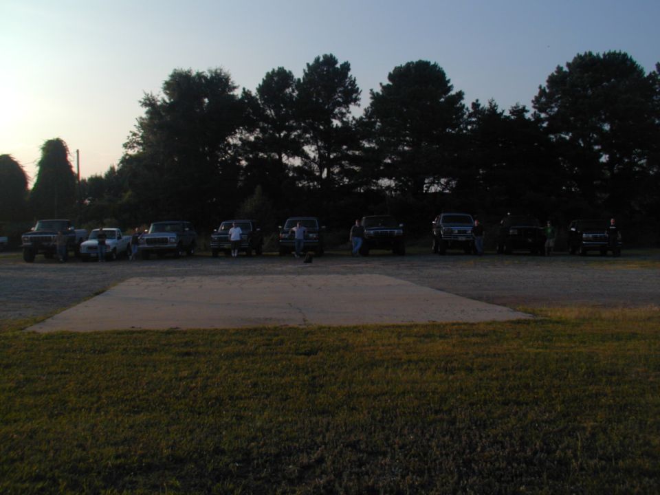 Several SUVs and trucks parked in a lot at dusk, with trees in the background