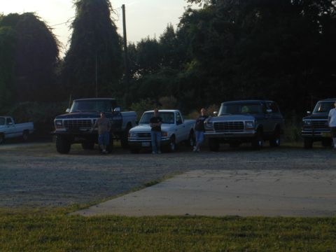 1988 Ford Bronco - A group of people pose with their Ford Bronco and pickup trucks in an outdoor lot.