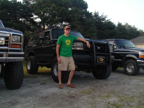 1988 Ford Bronco - Three Ford trucks are parked outside with a man posing next to a black Bronco.