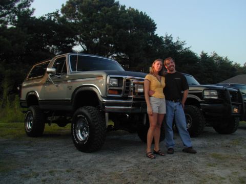1988 Ford Bronco - A couple stands next to a lifted Ford Bronco with another truck visible in the background.