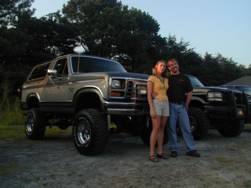 Couple posing with lifted Ford Bronco and another truck behind it