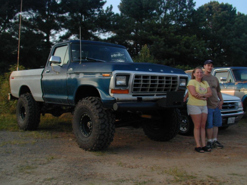 Blue and white Ford F-Series truck with large tires, lifted suspension, and a man and woman standing beside it