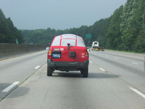 1988 Ford Bronco - A red SUV is seen from behind on a highway, its rear window covered by a tarp.