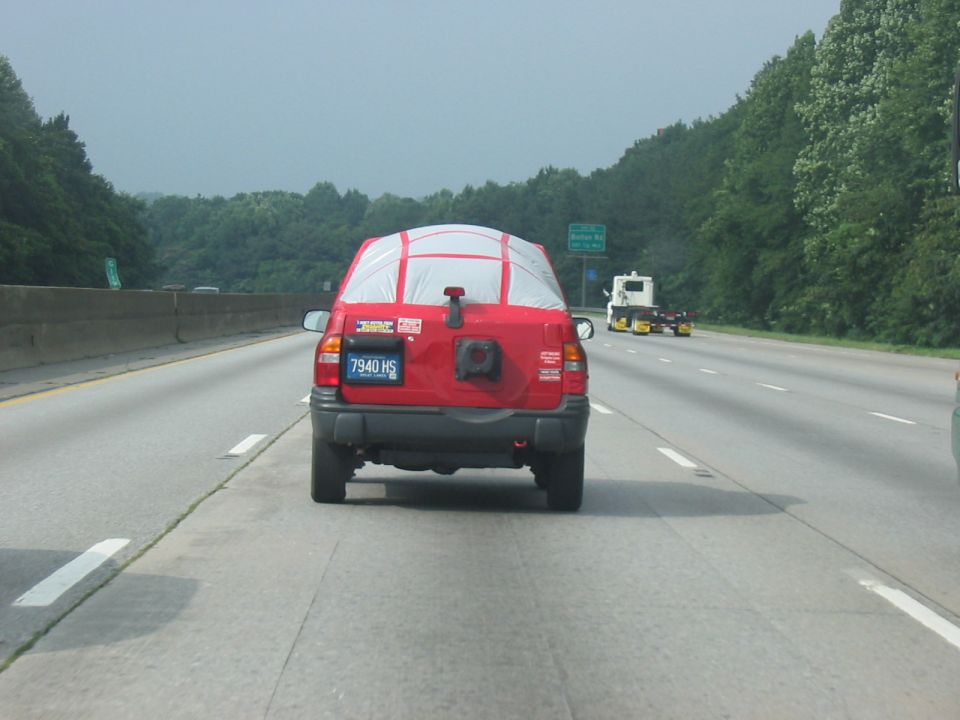 Red SUV with tarp on rear window, spare tire mount, and license plate 7940 HS