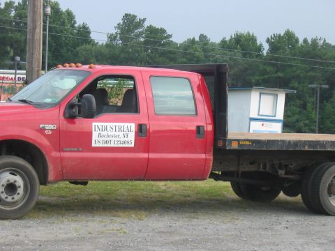 1988 Ford Bronco - A red crew cab flatbed truck is seen from the side, an "INDUSTRIAL Rochester, NY US DOT 1234085" decal on the door.