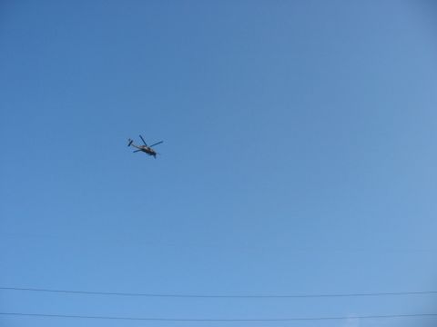 1988 Ford Bronco - A helicopter is seen in flight against a bright blue sky, with power lines visible below.
