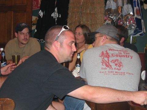 1988 Ford Bronco - A group of people are seated around a table, some with drinks, in what appears to be a casual gathering spot with a hay bale wall.