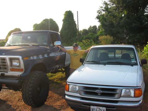1988 Ford Bronco - A man poses between a lifted dark blue Ford pickup and a white compact Ford pickup.