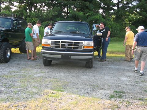1988 Ford Bronco - A group of men gather around a dark blue Ford Bronco parked outdoors on a gravel lot.