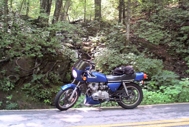 Blue Suzuki motorcycle parked on the side of a wooded road