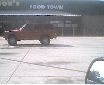 1988 Jeep Cherokee - Side view of a red 1988 Jeep Cherokee parked in a lot outside a Food Town store.