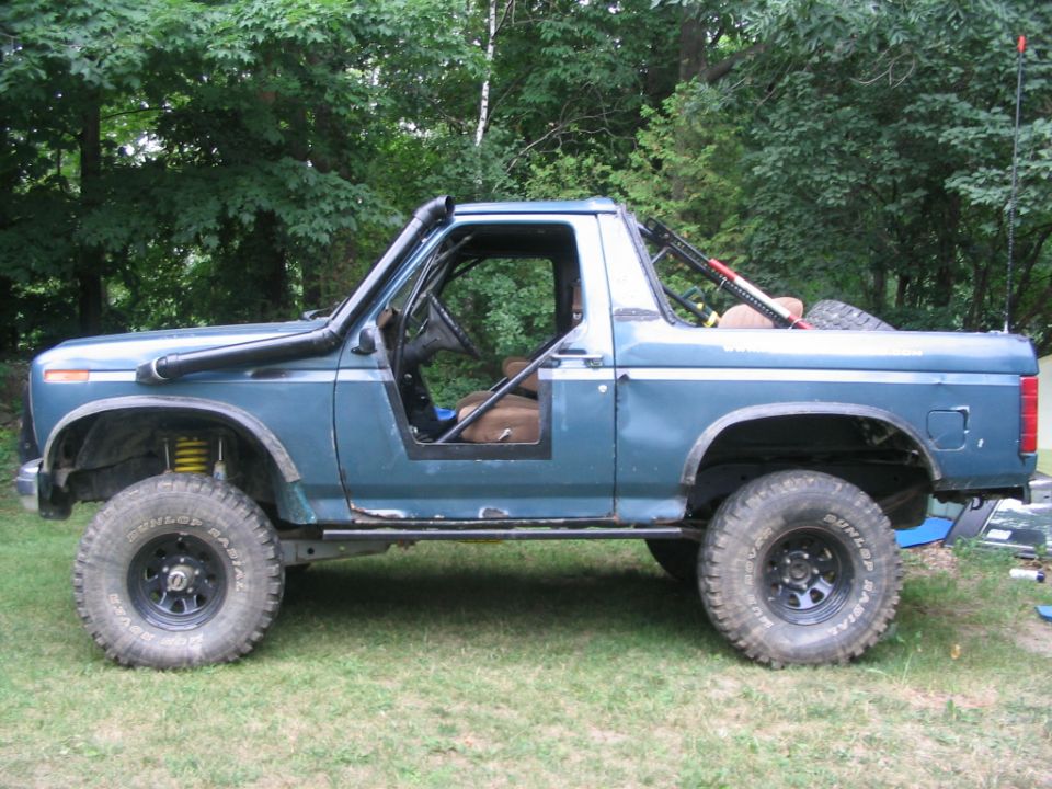 Blue topless Ford Bronco with snorkel and lift on mud tires, side view on grass