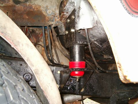 1979 Ford Bronco - Close-up of a suspension component with red and black bushings mounted to a heavily rusted frame.