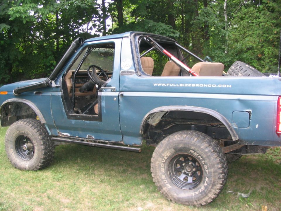 Lifted blue Ford Bronco with top removed, roll cage, snorkel and cut rear fenders on grass
