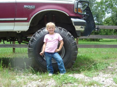 1993 Ford Bronco - A young girl poses in front of a lifted Ford Bronco with massive tires.