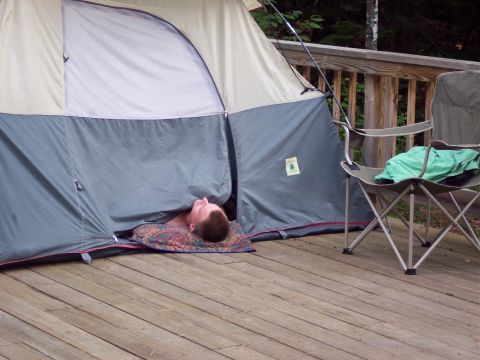 2001 Ford Crown Victoria - A person is resting inside a tent set up on a wooden deck next to a folding chair.