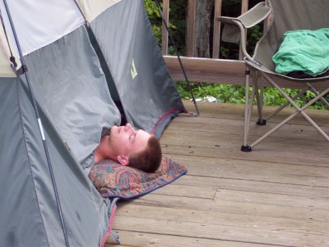 2001 Ford Crown Victoria - A person rests inside a tent pitched on a wooden deck, with a camping chair nearby.