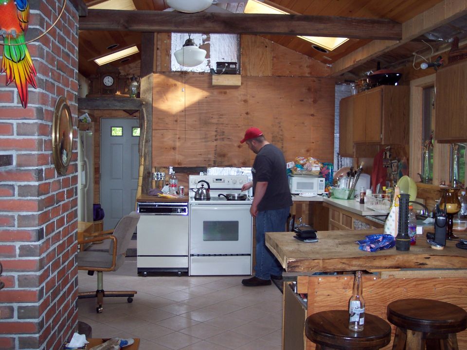 Kitchen scene with a man cooking at a stove, brick wall, wooden beams, and skylights