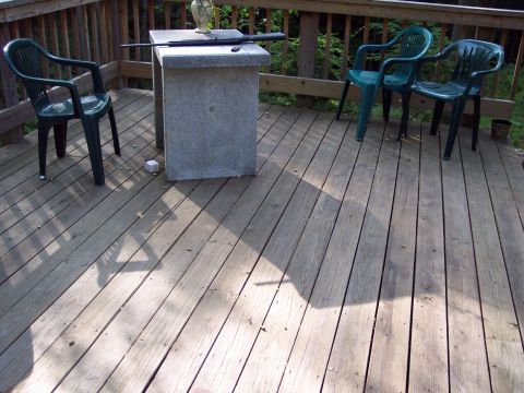 2001 Ford Crown Victoria - A rifle rests on a table on a wooden deck, flanked by three plastic chairs and a vase.