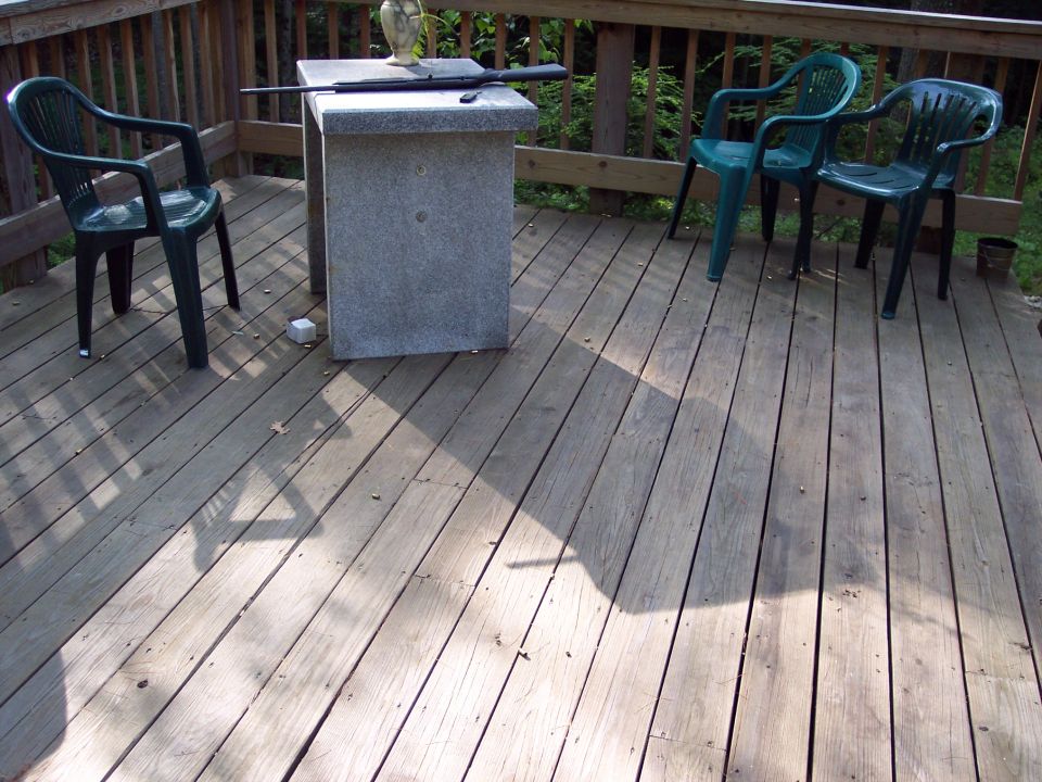 Deck scene with rifle on table, three chairs, and vase