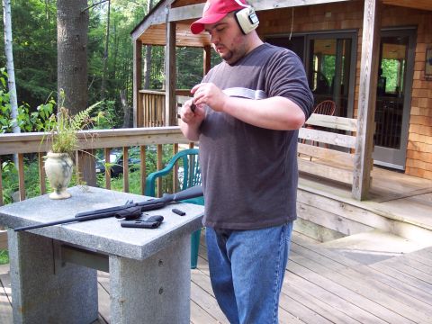 2001 Ford Crown Victoria - A man prepares firearms on a table on a wooden deck, with a cabin in the background.