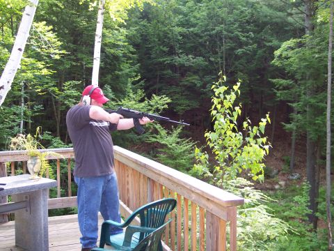 2001 Ford Crown Victoria - Man on a deck aims a rifle, with a dense forest visible behind him.
