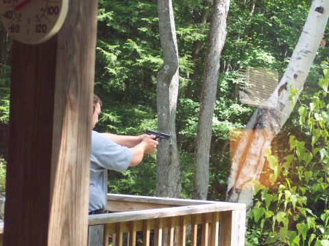 2001 Ford Crown Victoria - A man practices shooting a handgun outdoors on a wooden deck surrounded by trees.
