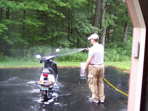 2001 Ford Crown Victoria - A man washes a scooter in a driveway with trees in the background.