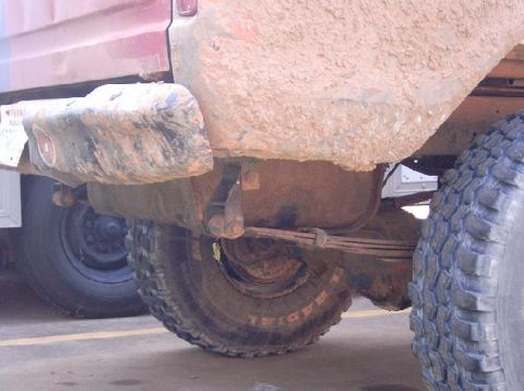 1978 Ford Bronco - Ground-level view under the rear of a mud-caked lifted 4x4, looking past the rear axle, leaf spring and shock to a spare tire mounted under…