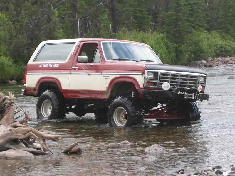 Lifted red and white Ford Bronco with winch bumper standing in a shallow river