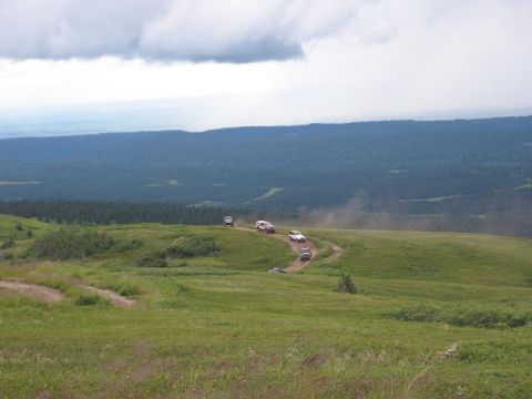 1985 Ford Bronco - Multiple SUVs navigate a dusty trail on a scenic mountain overlook.