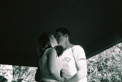 1988 Ford Bronco - A couple shares a kiss outdoors, with foliage visible behind them and a dark structure overhead.