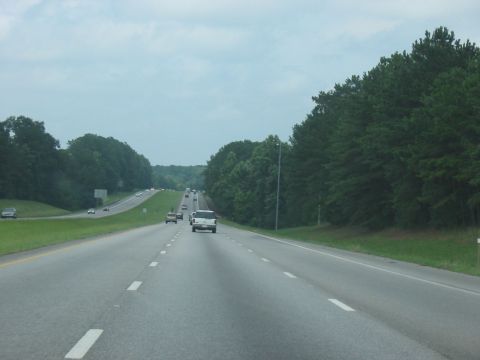 1988 Ford Bronco - A white pickup truck travels down a highway on a cloudy day, with dense trees visible on the right side of the road.