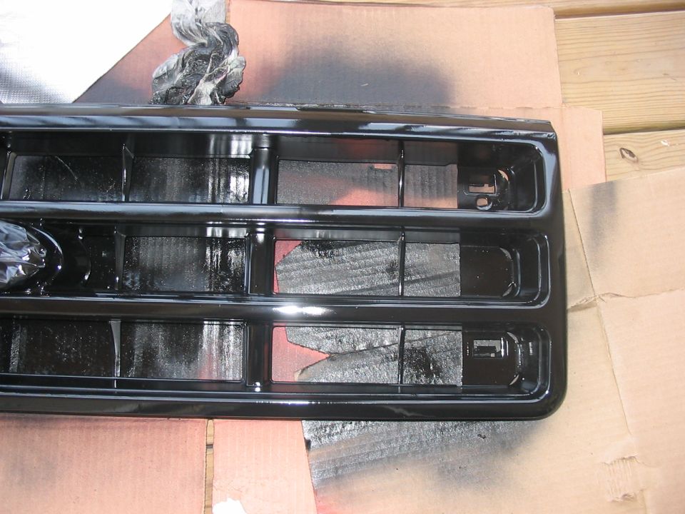 Black grille with horizontal bars, being spray painted black. Cardboard and wood planks visible