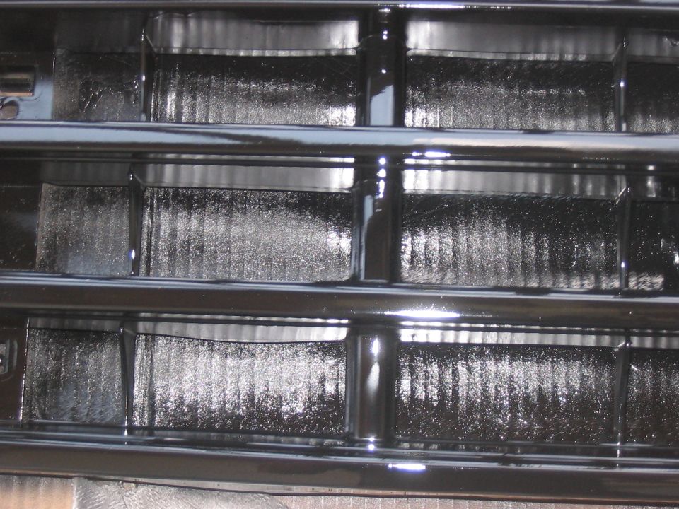 Close-up of a black vehicle grille with horizontal bars and textured inserts. Supermotors.net logo visible at bottom right
