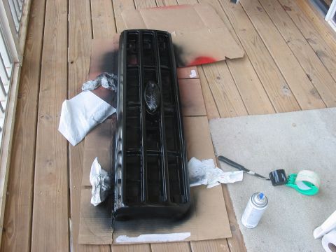 1988 Ford Bronco - A black Ford Bronco grille is being spray-painted on a wooden deck.
