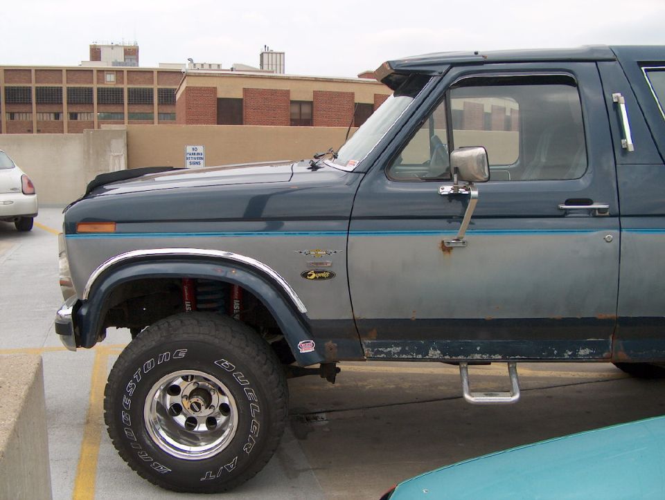 Side view of lifted two-tone blue/gray Ford Bronco with big Bridgestone tires in a parking garage