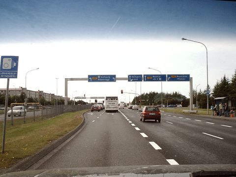 1996 Ford Bronco - A red car travels down a highway with multiple traffic signs overhead and other vehicles present.