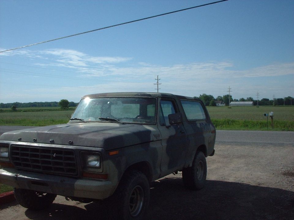 Ford Bronco with camouflage paint, parked on dirt road