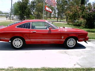 1978 Ford Mustang II - Side view of a red coupe with American flags in the background.