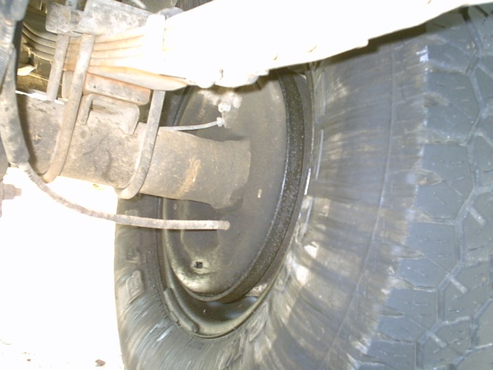 Close-up of a vehicle's rear axle, leaf springs, brake drum, and tire