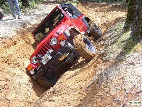 1984 Ford Bronco - A red Jeep Wrangler is stuck at an extreme angle in a deep dirt ditch during off-road driving.
