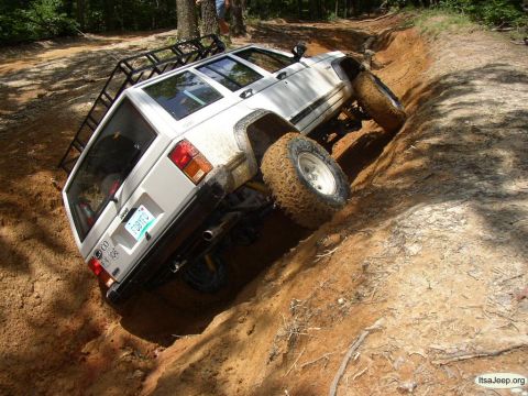 1984 Ford Bronco - A white Jeep Cherokee XJ navigates a steep, muddy incline during an off-road excursion.