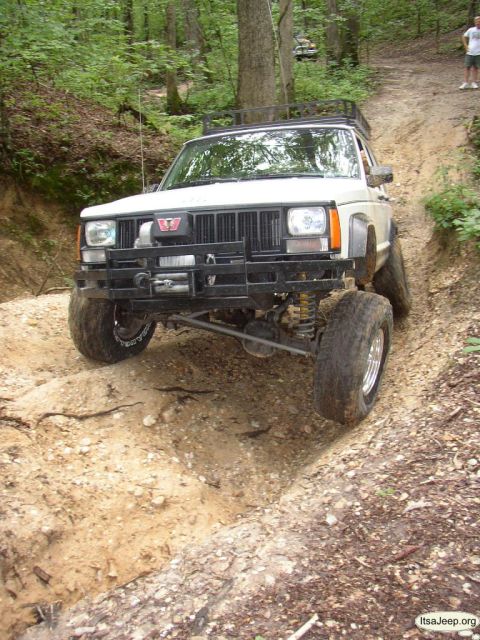 1984 Ford Bronco - A white Jeep Cherokee XJ navigates a steep dirt trail during an off-road excursion.