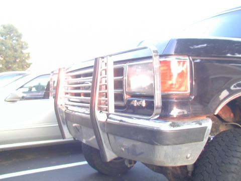 1988 Ford Bronco - Front view of a black Ford truck with a chrome brush guard and 4x4 badging, parked beside a white vehicle.