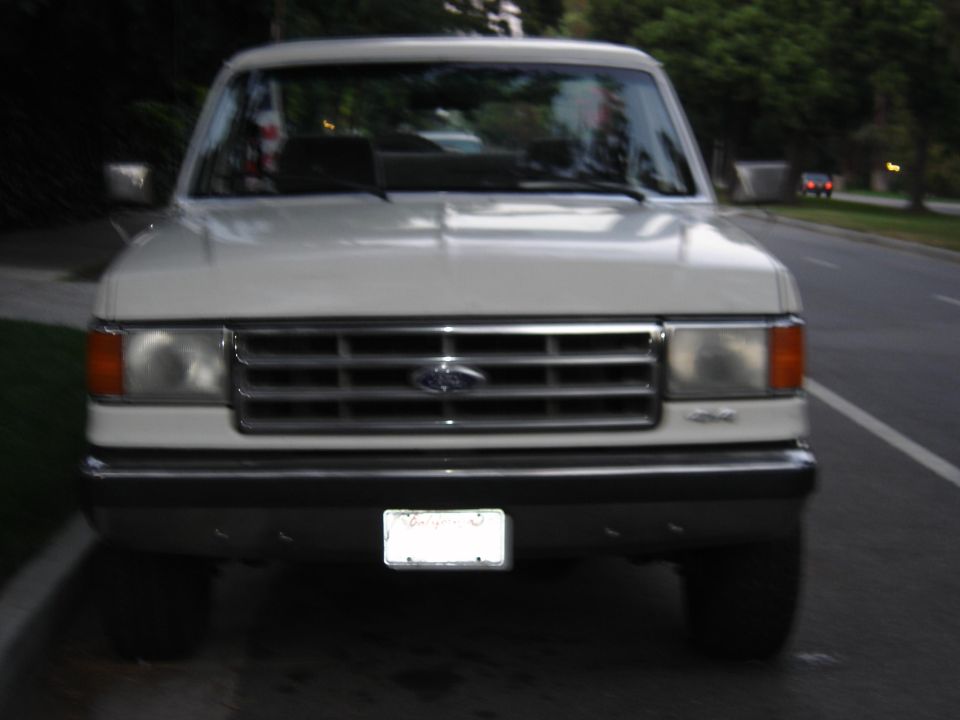 Front view of a white late-1980s Ford 4x4 with chrome grille parked at a curb