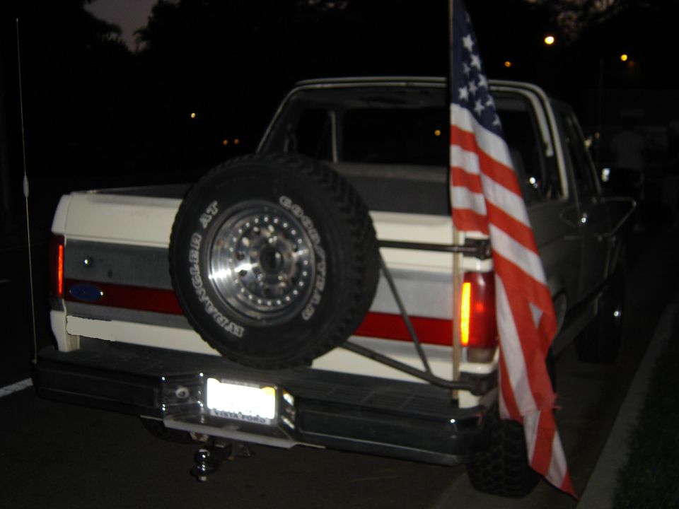 Rear of white Ford Bronco at dusk with swing-out spare tire carrier and American flag
